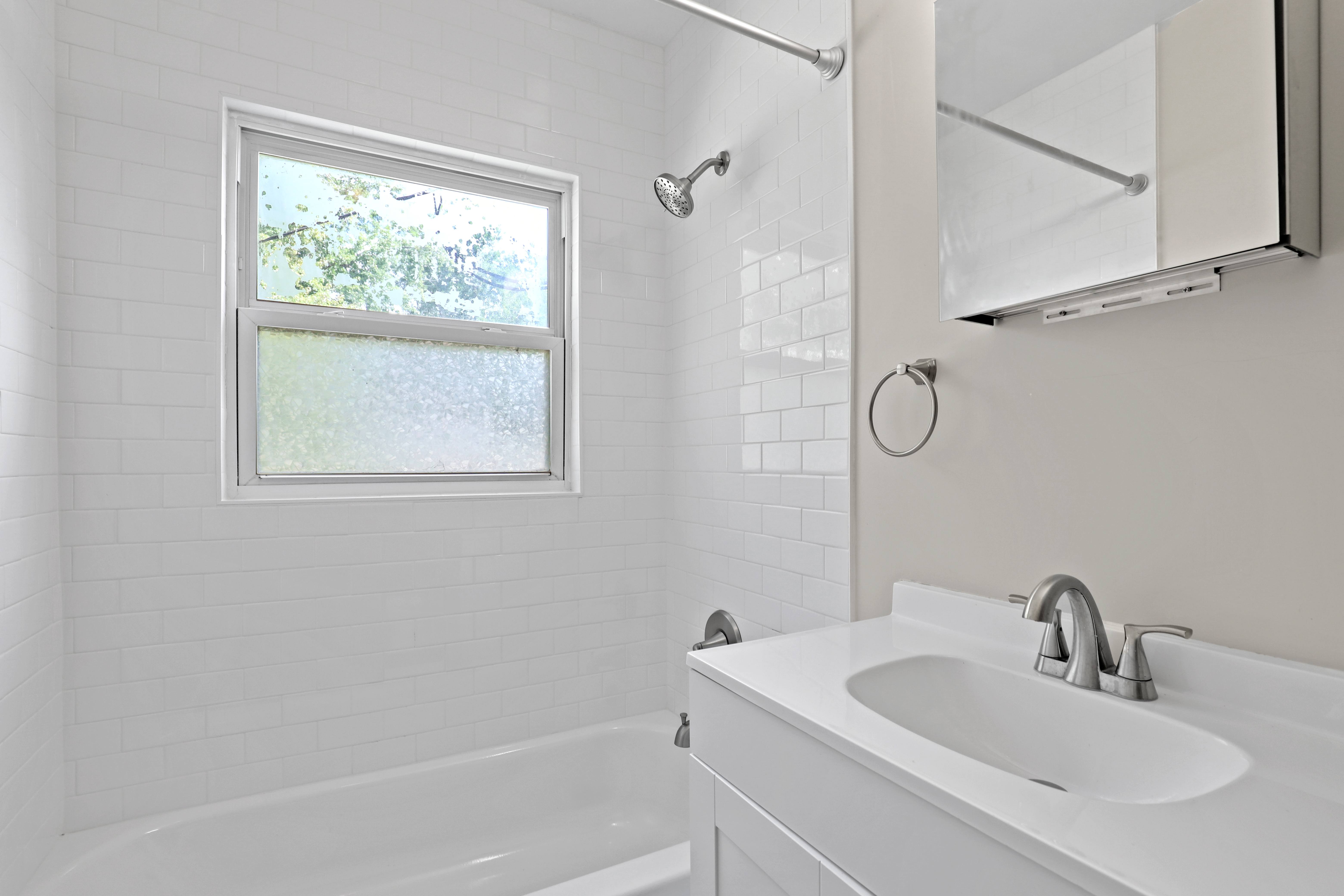 a white bathroom with a sink and a tub and a window